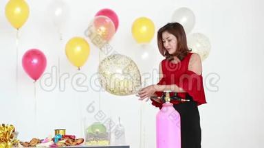 亚洲女人穿着红色衬衫，用<strong>气球</strong>泵吹闪闪发光的<strong>气球</strong>，身后有五颜六色的<strong>气球</strong>，是聚会的概念。